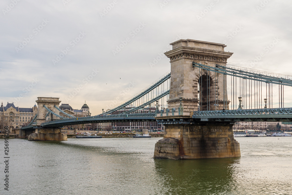 Obraz premium Chain Bridge with Danube river flowing under it as seen from riverside od Danube river in Budapest, Hungary.