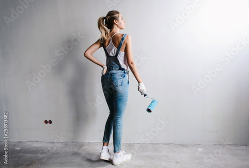 Happy beautiful smiling woman with roller in her hand painting interior wall of new house. New flat renovation concept. White background copyspace