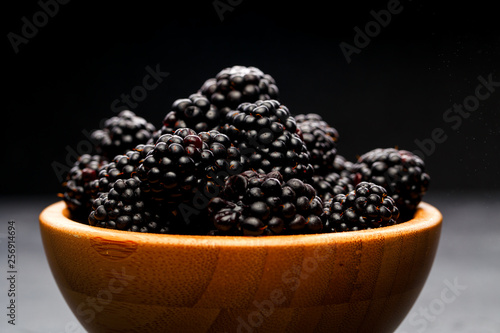 Photo of blackberry in wooden cup on empty black background.