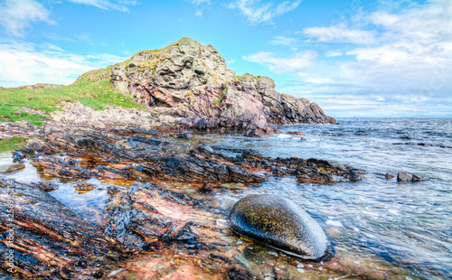 Photography Jagged rock layers and boulders smoothed by the ocean are seen at an intertidal zone on the island of Islay, Scotland, UK