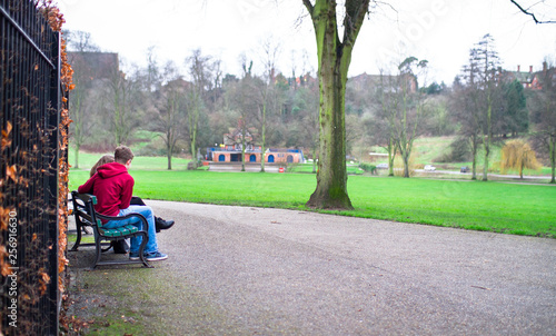 A young couple sits on a park bench in Shrewsbury, Shropshire, England.