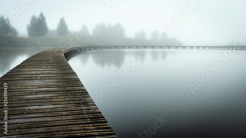 Tablou pe pânză Boardwalk over still water in the fog
