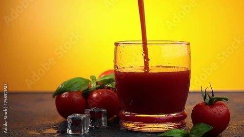 Pouring tomato bloody mary cocktail in drinking glass with water drops on dark blue concrete table with spot light. Yellow background.
