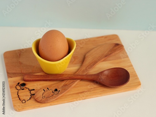 Handmade kitchen wooden board, spoon and egg in coddler on light background