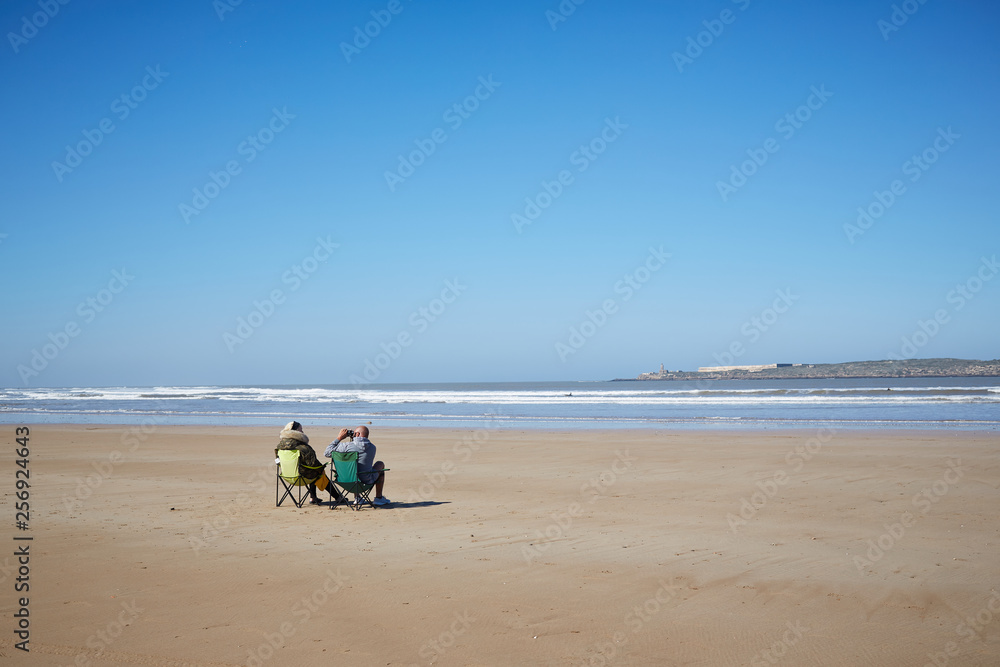 Ein Paar sitzt am leeren Strand und schaut mit dem Fernglas 
