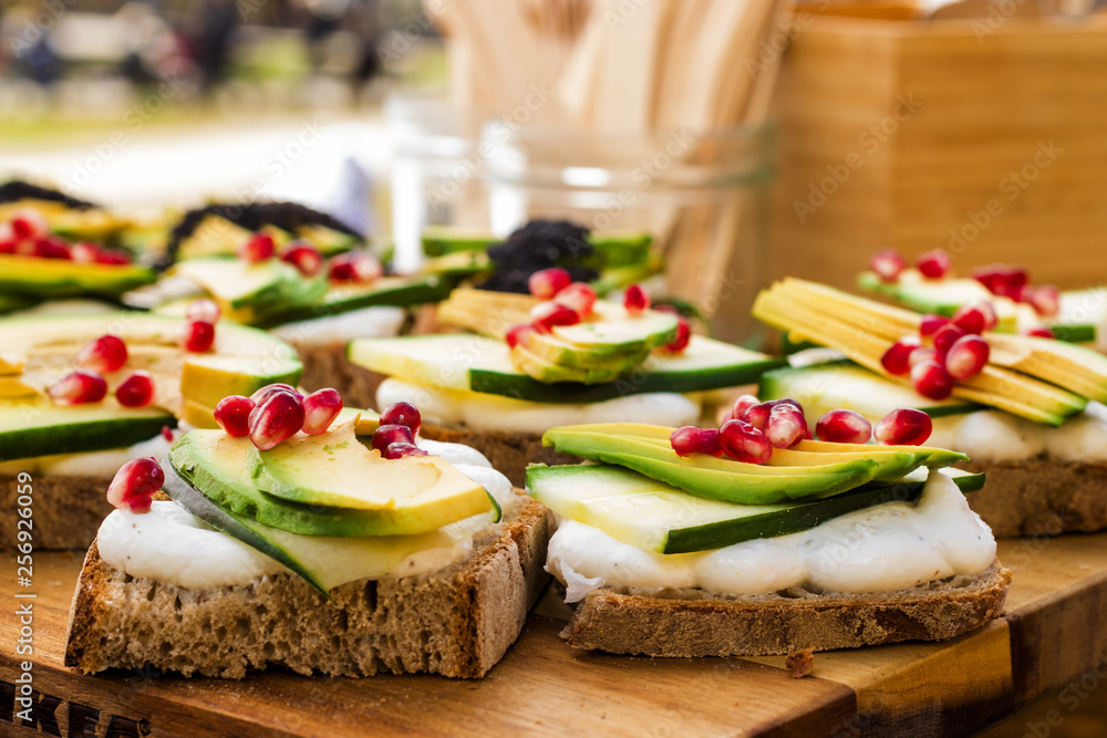 Avocado Sandwich with Feta cheese - sliced avocado and Feta cheese on bread with arugula leaves, embellished with pomegranate pips and sesame seeds for healthy breakfast or snack.