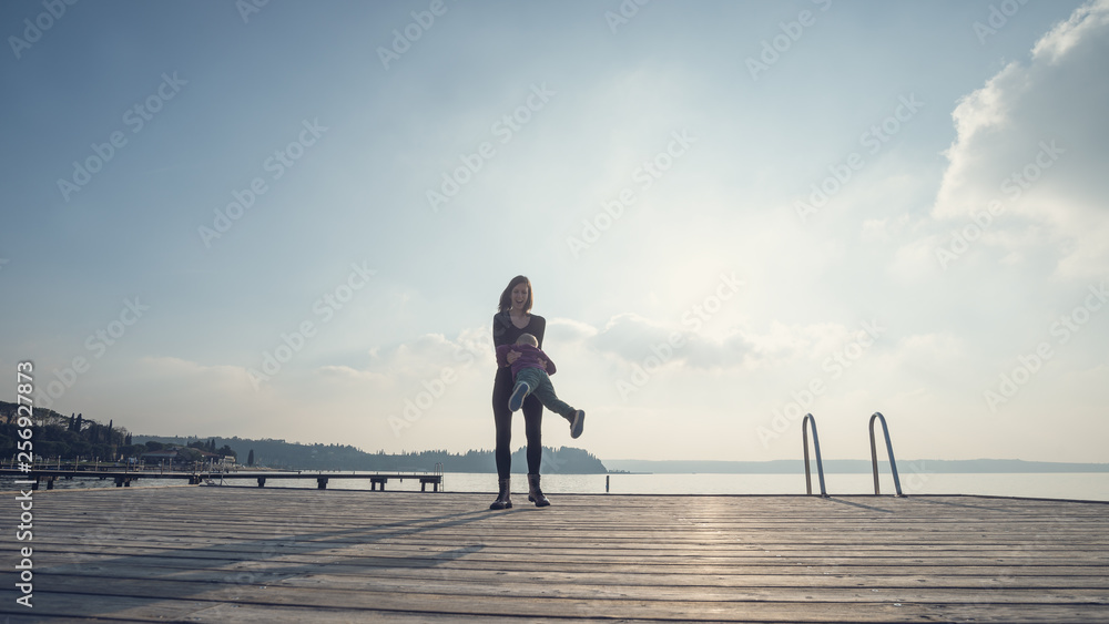 Happy young mother standing on wooden pier spinning her son