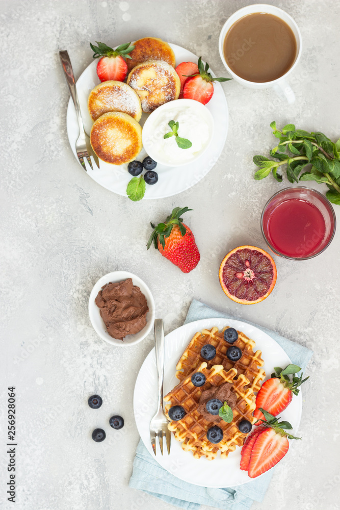 Belgian waffles with chocolate sauce, berries and mint and cottage cheese pancakes on a light gray background. Breakfast or lunch. Copy space.