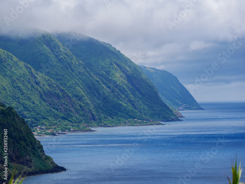 Image of cloudy and foggy coastline with green mountains full of trees and forest on the island of Sao Jorge, Azores, Portugal, Europe