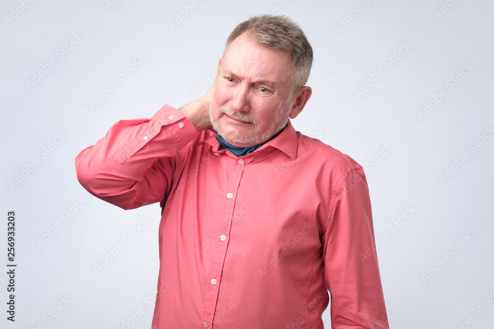 Frustrated senior man in red shirt holding hand on his neck Frustrated senior man in red shirt holding hand on his neck