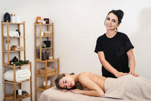Beautiful young slim woman lying with closed eyes and waiting for massage in spa. Young female friendly massagist standing and looking to the camera. Beauty, spa, healthy lifestyle and relaxation photo