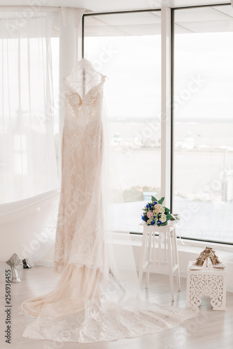 Wedding dress of the bride. The bride's dress hangs on a hanger near the window.