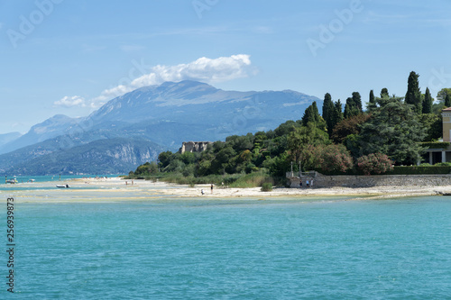 Stony Beach of Sirmione town on Garda Lake with view of Grottoes of Catullus (Grotte di Catullo), the ruins of a Roman villa built at the end of the 1st century B.C. View from Garda Lake. photo