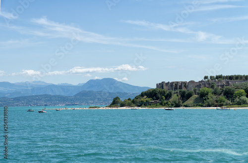 Stony Beach of Sirmione town on Garda Lake with view of Grottoes of Catullus (Grotte di Catullo), the ruins of a Roman villa built at the end of the 1st century B.C. View from Garda Lake.