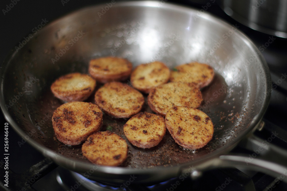 Red potato potato chips cooking in a stainless steel pan.
