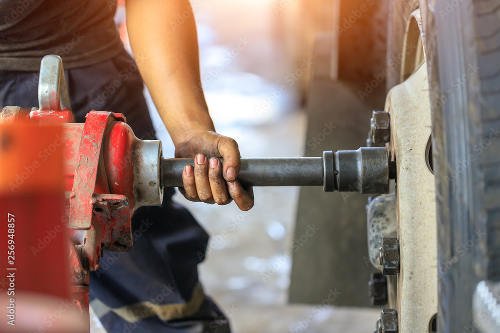 Close up of Truck Wheel mechanic hands using a pneumatic gun to loosen a wheel nut in a mechanical workshop in the Truck Service Center,spot focus. Close up of Truck Wheel mechanic hands using a pneumatic gun to loosen a wheel nut in a mechanical workshop in the Truck Service Center,spot focus.