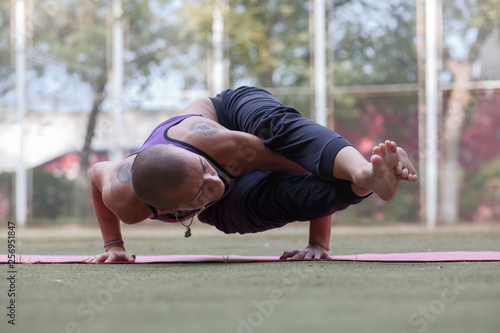 tattooed skinhead woman in Eight-Angle yoga Pose, Astavakrasana,  on green lawn in summer park photo