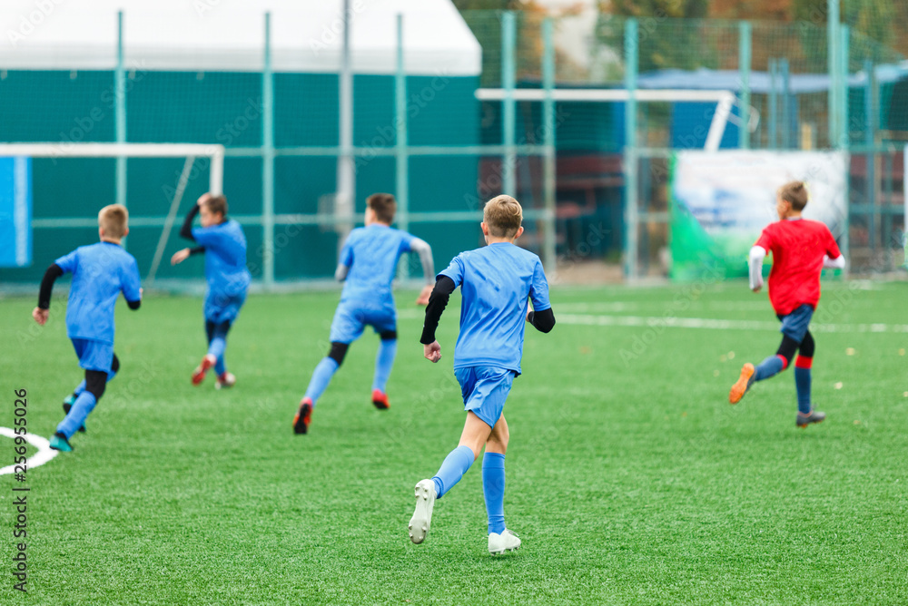 Fototapeta premium Football training for kids. Boys in blue red sportswear on soccer field. Young footballers dribble and kick ball in game. Training, active lifestyle, sport, children activity concept 