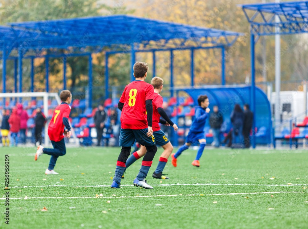 Boys in red white blue sportswear running on soccer field. Young footballers dribble and kick football ball in game. Training, active lifestyle, sport, children activity concept Boys in red white blue sportswear running on soccer field. Young footballers dribble and kick football ball in game. Training, active lifestyle, sport, children activity concept