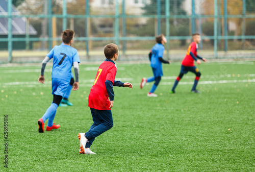 Boys in red white blue sportswear running on soccer field. Young footballers dribble and kick football ball in game. Training, active lifestyle, sport, children activity concept
