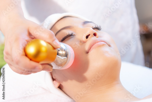 Rejuvenating facial therapy treatment at spa salon clinic. Young beautiful Asian woman getting lifting anti-aging, face massage and skincare by electroporation facial therapy aesthetic cosmetology. photo