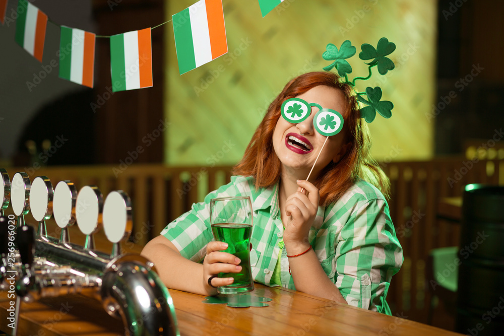 Red-haired pretty girl in a green checkered shirt having fun with eyewear with shamrock symbols