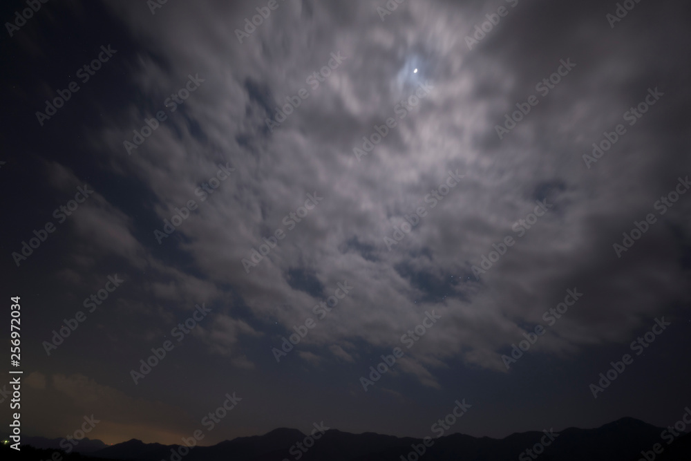 Obraz premium 躍動感のある雲に隠れた月と原っぱ