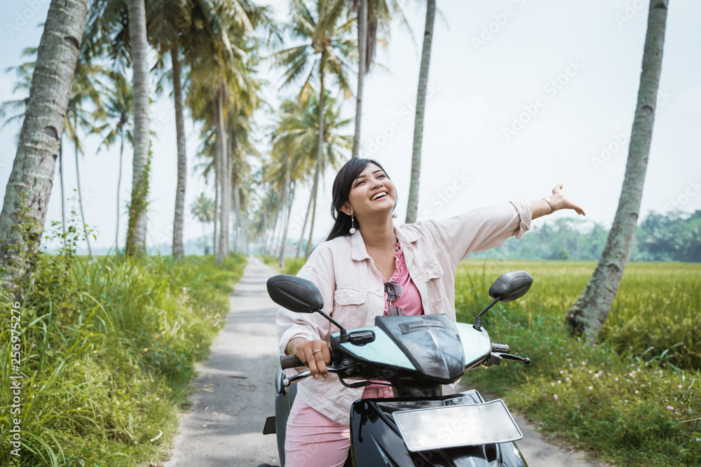young woman riding her scooter bike in tropical country road with coconut trees young woman riding her scooter bike in tropical country road with coconut trees