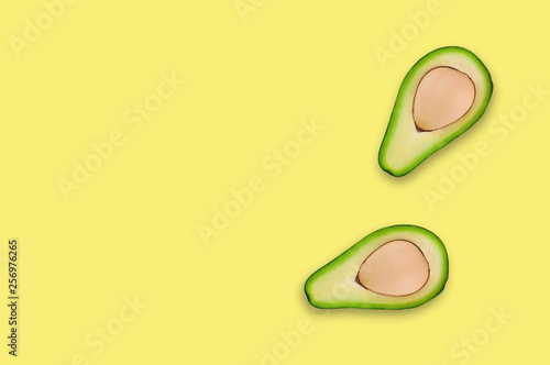 Two tasty fresh halves of organic avocado with kernels in center of yellow table in kitchen or market. Top view. Cooking concept. Copy space for your text