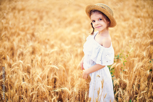 Happy child in autumn wheat field. Beautiful girl in white dress and straw hat have fun with playing, harvesting wheat.