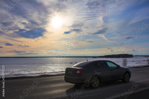 car moves along the road along the winter frozen lake