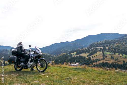 Fototapeta Naklejka Na Ścianę i Meble -  A motorcyclist resting with his touristic motorcycle, with big bags ready for a long trip, black style, white helmet, ride, adventure, outdoor activities, mountains road, Romania