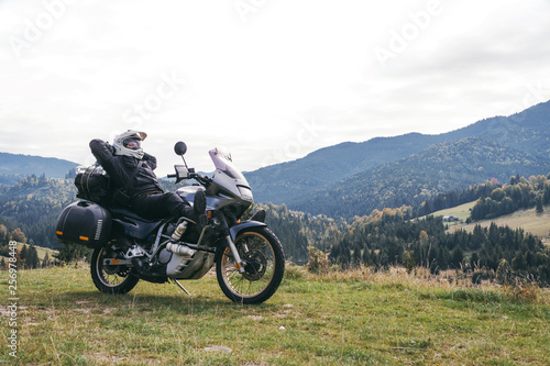A motorcyclist resting with his touristic motorcycle, with big bags ready for a long trip, black style, white helmet, ride, adventure, outdoor activities, mountains road, Romania
