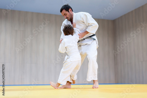 Judo kid and his trainer engaged in judo class in a dojo. Trainer teaches child the methods and techniques od ashi waza
