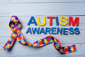 World Autism awareness and pride day or month with Puzzle pattern ribbon on blue wooden background.