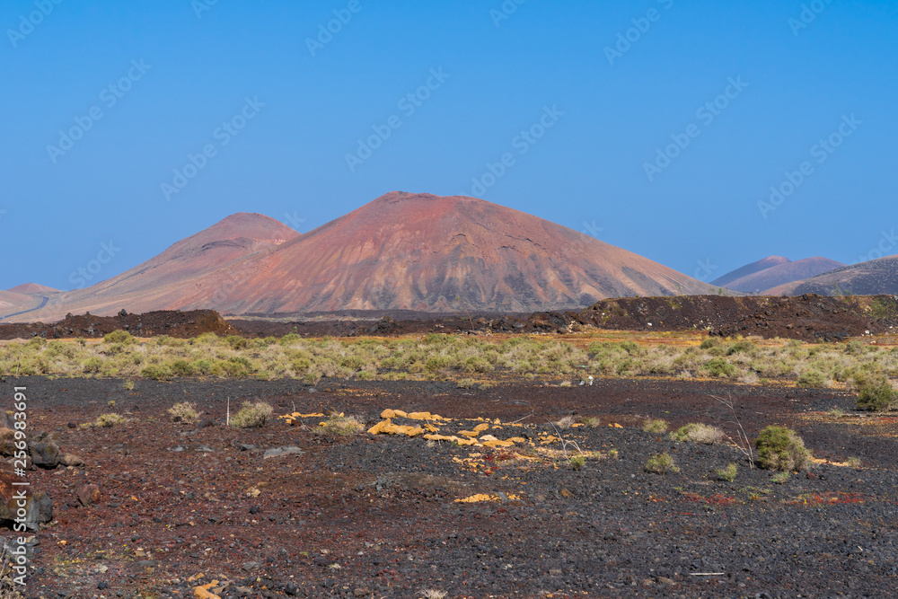 Spain, Lanzarote, Red volcanoes behind endless fields of volcanic soil