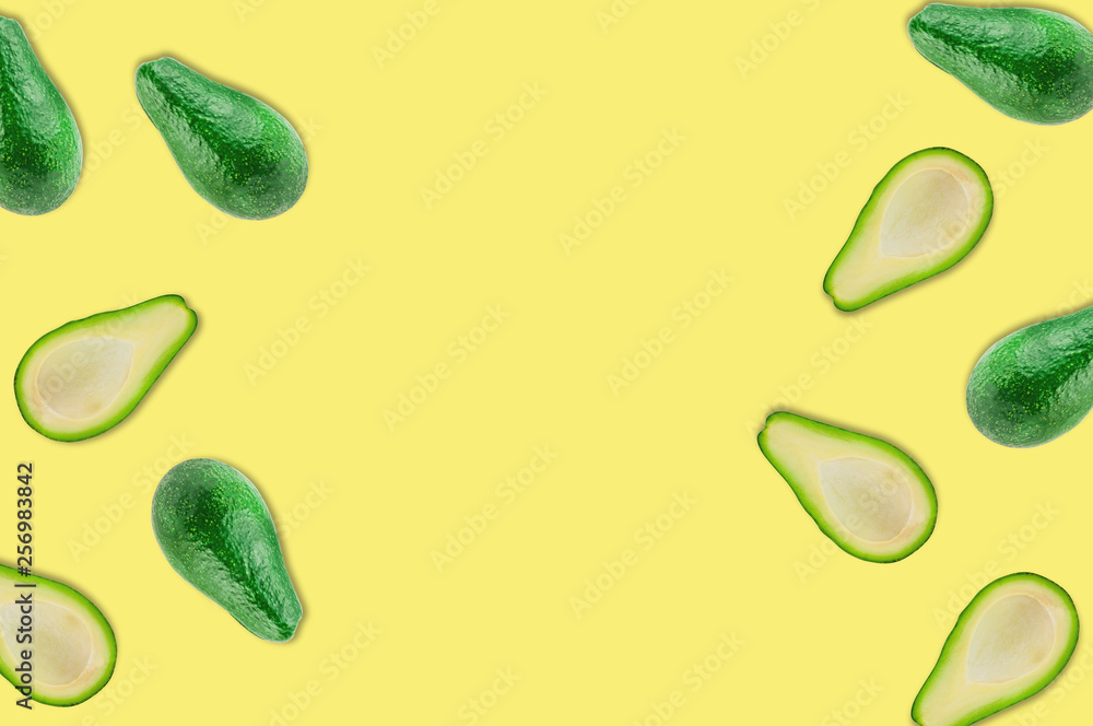 Scattered fresh wholes and halves of organic avocado without kernels on yellow table in kitchen or market. Top view. Cooking concept. Copy space for your text