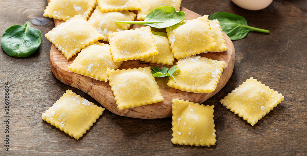 Tableau sur toile Tasty raw ravioli with flour and greens on dark background.