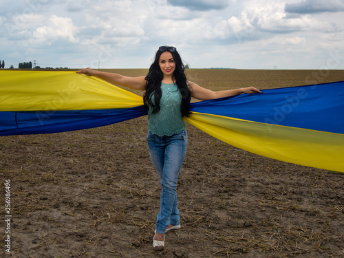 Young amazing beautiful girl with a huge Ukrainian flag on the field. Ukraine s Independence Day.