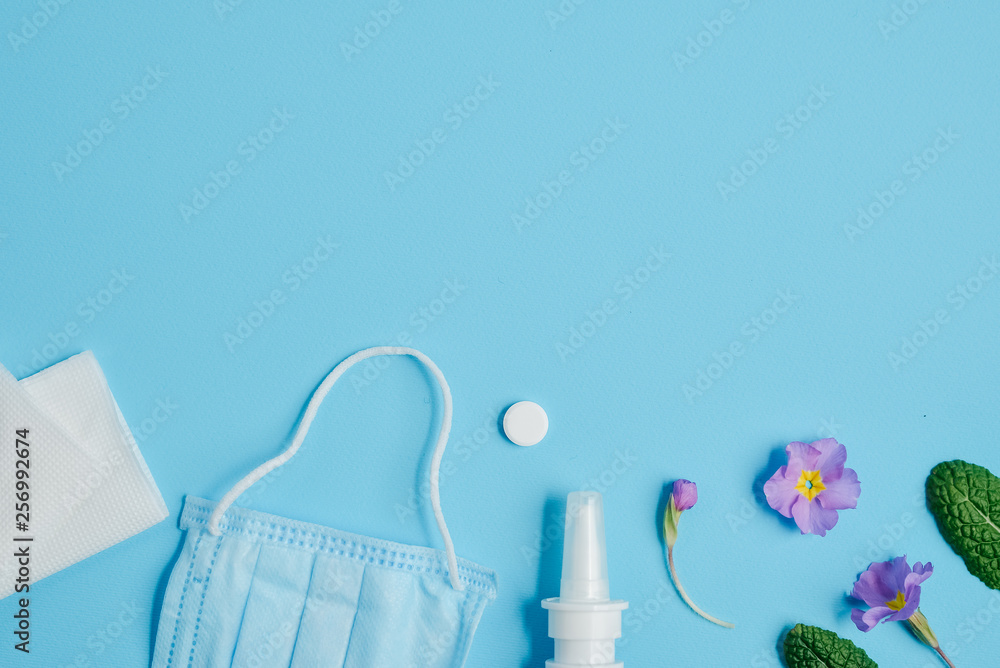 Workspace with napkins, pills, face mask, drops bottle and flowers on blue background. Creative flat lay concept of seasonal spring and summer pollen allergy. Top view, copy space, minimal style