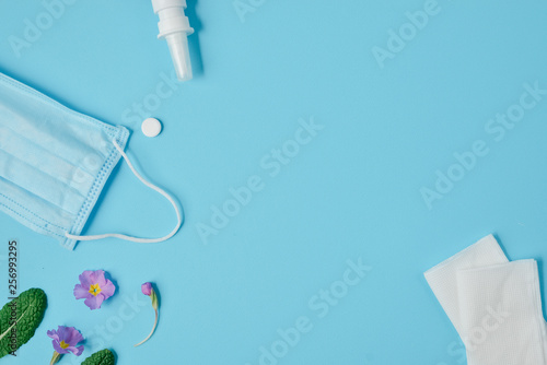 Workspace with napkins, pills, face mask, drops bottle and flowers on blue background. Creative flat lay concept of seasonal spring and summer pollen allergy. Top view, copy space, minimal style