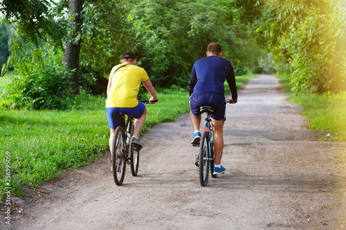 Cyclists spend their time on bicycles in park on sunny day among many trees. Ride for exercise and relaxation. Healthy lifestyle. Sport and active life concept.