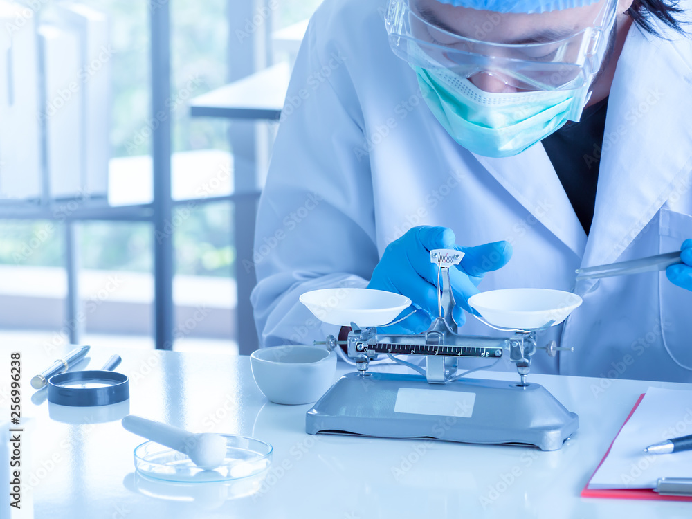 Fototapeta premium Close up, an asian chemist or scientist researcher using mechanical scale for gathering and measuring specimen at laboratory. The young man wearing safety glasses in experiment.