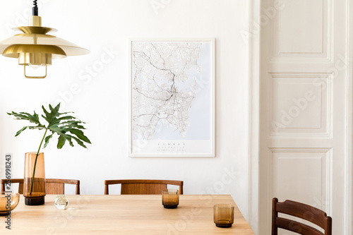 Fototapeta Stylish and modern dining room interior with mock up poster map, sharing table design chairs, gold pedant lamp and cups of coffee