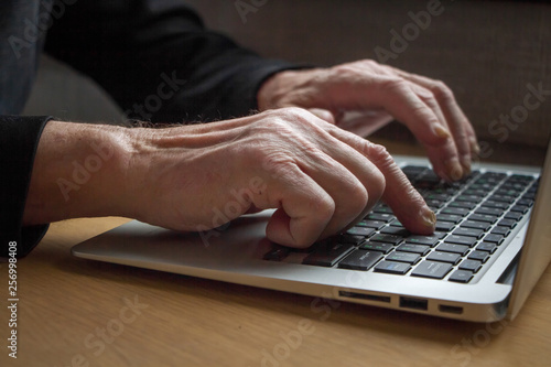The hands of an elderly person working on a laptop keyboard, typing, searching for information on the Internet.
