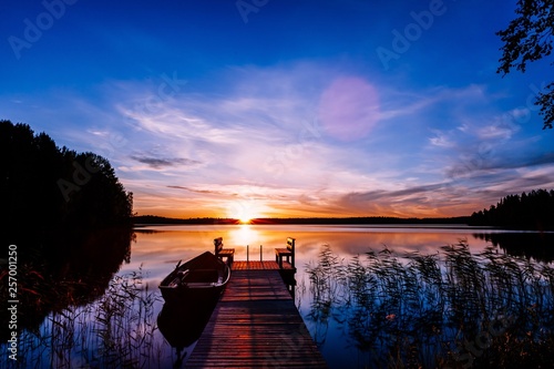 Wooden pier with fishing boat at sunset on a lake in Finland © nblxer