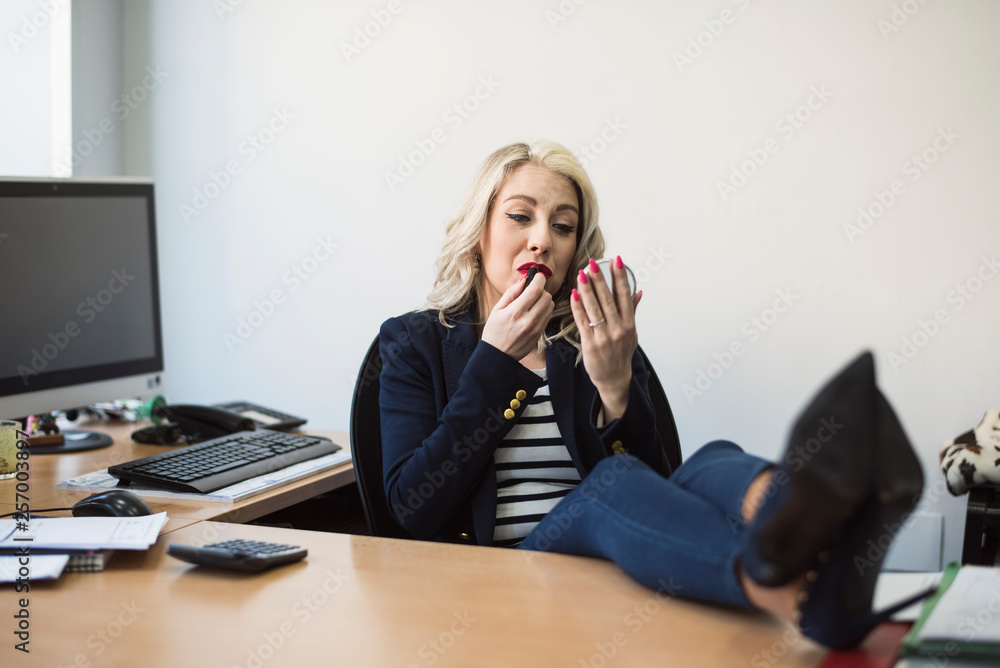Woman office worker puts makeup on and paints her lips during a break during working hours Woman office worker puts makeup on and paints her lips during a break during working hours