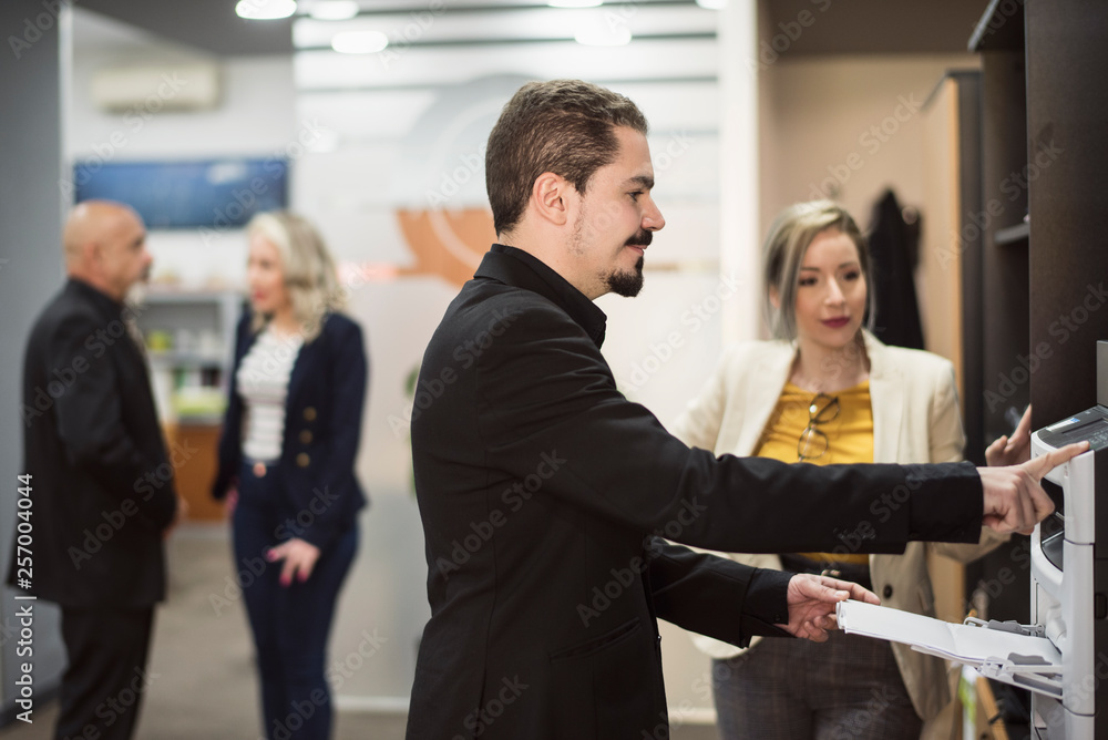 Man in office sending fax or printing files with people in background Man in office sending fax or printing files with people in background