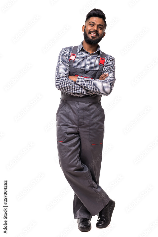 Fototapeta premium Portrait of cheerful indian repairer in shirt and overall having arms crossed looking at camera isolated on grey background