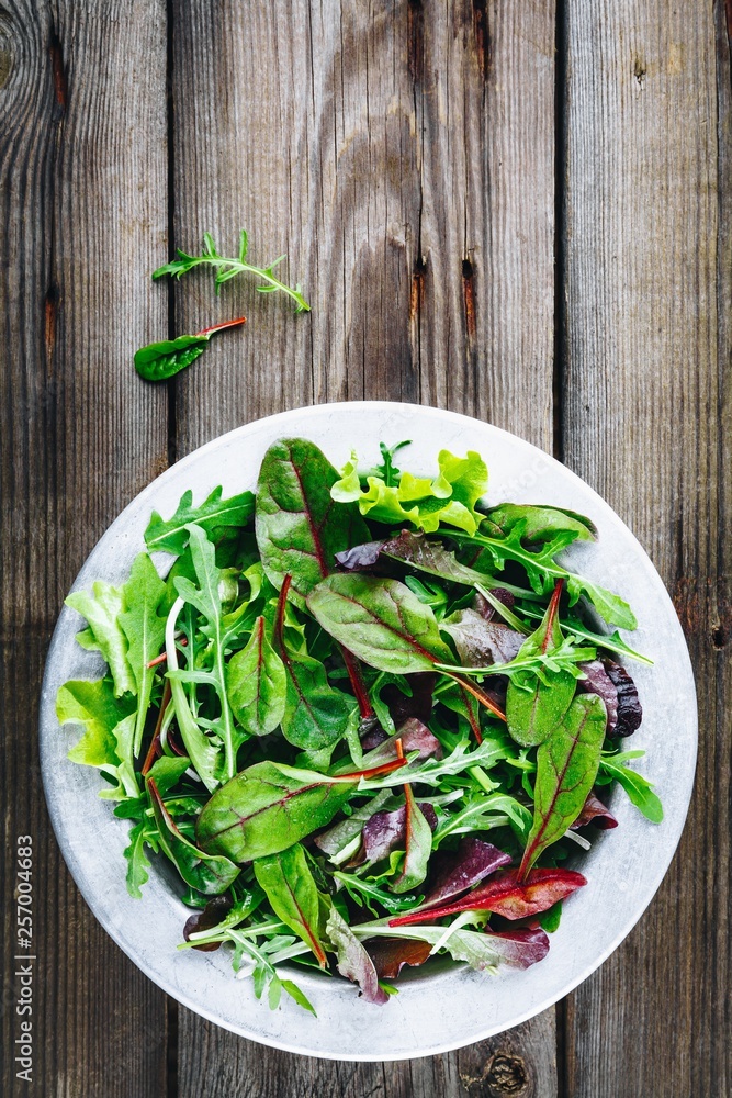 Fototapeta premium Mix of fresh leaves with arugula, lettuce, beets. Ingredients for salad on a wooden background.
